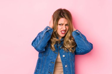 Pembe arka planda izole edilmiş genç beyaz kadın kulaklarını elleriyle kapatıyor..