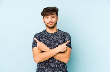 Mavi arka plan noktalarında izole genç bir Arap adam, iki seçenek arasında seçim yapmaya çalışıyor.