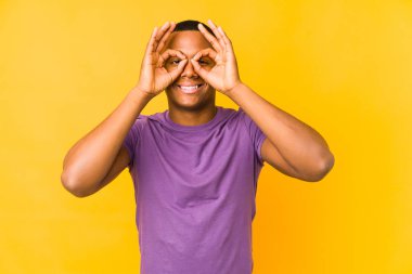 Sarı arka planda izole edilmiş genç latin adam gözlerde sorun olmadığını gösteriyor.