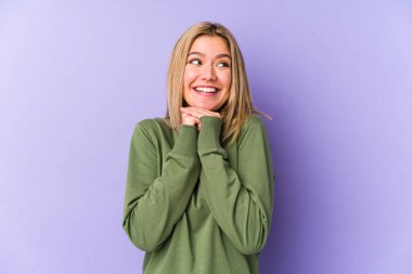 Sarışın, yalnız, beyaz bir kadın ellerini çenesinin altında tutuyor ve mutlu bir şekilde yan tarafa bakıyor..