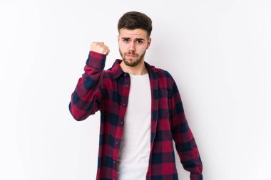 Beyaz arka planda poz veren beyaz tenli genç bir adam izole edilmiş kameraya yumruğunu gösteriyor, agresif bir yüz ifadesi var..