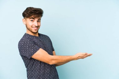 Mavi arka planda izole edilmiş genç bir Arap adam palmiyesinde bir kopya alanı tutuyor..