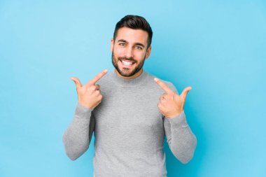 Mavi arka planda genç beyaz bir adam izole edilmiş gülücükler, dudaklarını işaret ediyor..