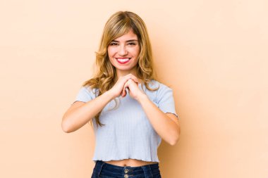 Sarışın, beyaz bir kadın ellerini çenesinin altında tutuyor ve mutlu bir şekilde yan tarafa bakıyor..