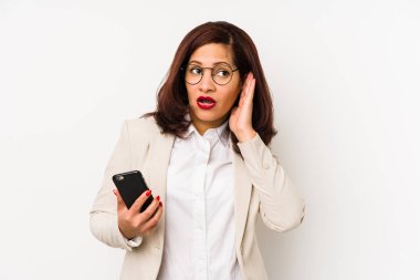 Orta yaşlı, elinde cep telefonu olan Latin bir kadın bir dedikoduyu dinlemeye çalışıyor..