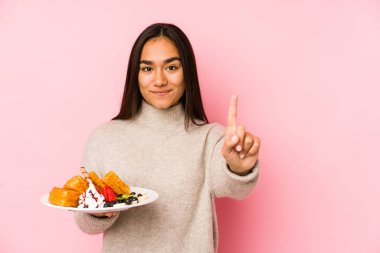 Genç Asyalı kadın bir waffle tutuyor. Bir numarayı parmağıyla gösteriyor..