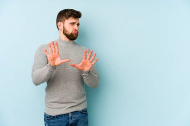 Mavi arka planda izole edilmiş genç beyaz adam tiksinti belirtisi gösteren birini reddediyor..