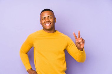 Mor arka planda izole edilmiş genç latin adam zafer işareti gösteriyor ve gülümsüyor..