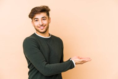 Bej bir arka planda izole edilmiş genç bir Arap adam palmiyesinde bir kopya alanı tutuyor..