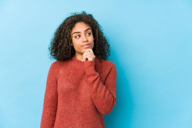 Genç Afro-Amerikan kıvırcık saçlı kadın şüpheli ve şüpheci bir ifadeyle yana bakıyor..