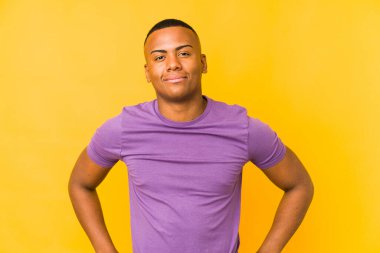 Sarı arka planda izole edilmiş genç latin adam ellerini kalçasında tutuyor..