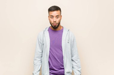 Genç Güney Asyalı adam omuz silker ve gözleri açık kalır..