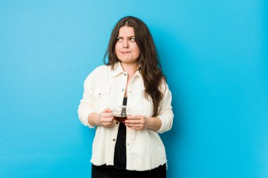 Elinde çay fincanı tutan kıvrımlı genç kadın kafası karışmış, şüpheli ve kararsız hissediyor..