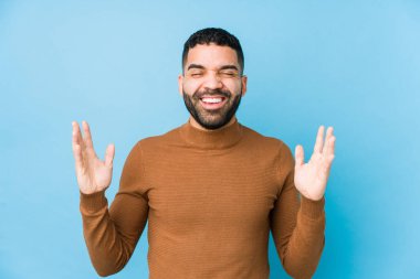 Mavi arka planda genç bir latin adam neşeli bir şekilde gülüyor. Mutluluk kavramı.