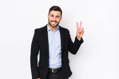 Beyaz arka planda beyaz tenli genç beyaz bir iş adamı zafer işareti gösteriyor ve gülümsüyor..