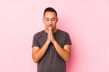 Pembe arka planda poz veren, ağzı yakın dua eden, kendinden emin Latin bir adam..