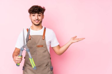 Genç Arap bahçıvan, avucunun içinde bir kopya alanı gösterip belinde bir el daha tutuyor..