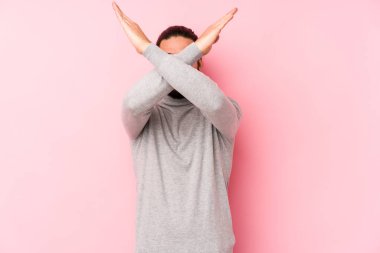 Genç, uzun saçlı adam pembe arka planda izole edilmiş iki kolu çapraz tutuyor, inkar kavramı..
