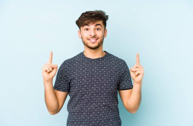 Mavi bir arka planda izole genç bir Arap adam işaret iki ön parmakları boş bir boşluk gösteren.