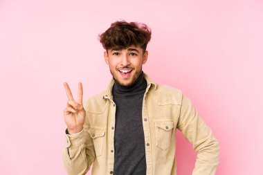 Arka planda poz veren genç bir Arap adam neşeli ve tasasız bir şekilde parmaklarıyla barış sembolü gösteriyor..