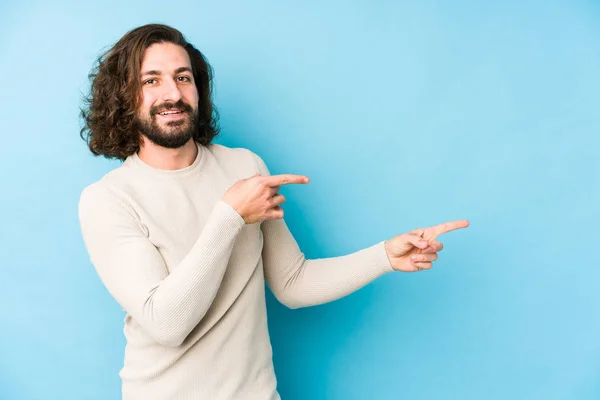 Giovane Uomo Capelli Lunghi Isolato Uno Sfondo Blu Eccitato Indicando — Foto Stock