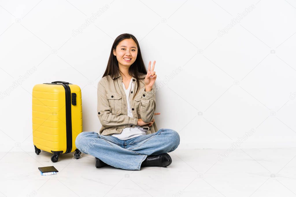 Young chinese traveler woman sitting holding a boarding passes showing number two with fingers.