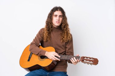 Gitar çalan genç beyaz adam mutlu, güler yüzlü ve neşeli..
