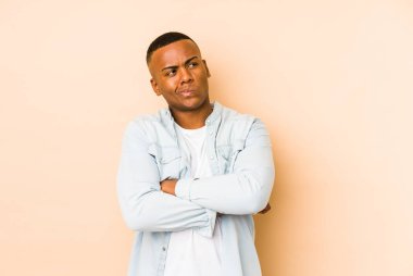 Genç latin adam bej arka planda izole edilmiş hoşnutsuzca kaşlarını çatmış, kollarını kavuşturmuş..