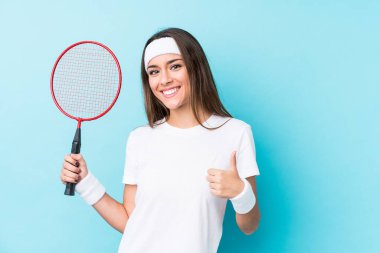 Badminton oynayan beyaz kadın kendini izole edip gülümsüyor ve başparmağını kaldırıyor.