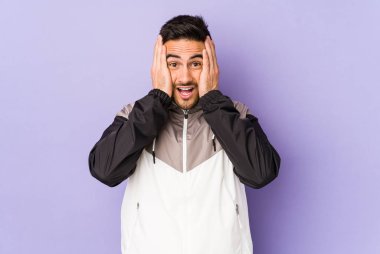 Mor arka planda izole edilmiş genç beyaz adam yüzünün yarısını palmiye ile kaplayarak eğleniyor..