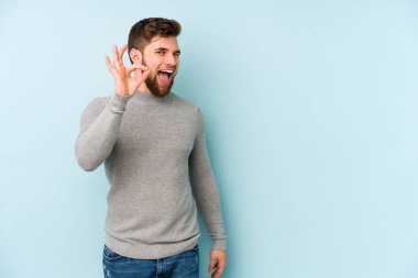 Kafkasyalı genç adam mavi arka planda izole edilmiş neşeli ve kendinden emin..