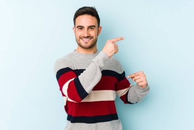 Kafkasyalı genç adam mavi arka planda izole edilmiş. Elinde işaret parmaklarıyla küçük bir şey tutuyor, gülümsüyor ve kendinden emin..