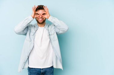 Mavi arka planda izole edilmiş genç beyaz adam gözlerinde sorun olmadığını gösteriyor.