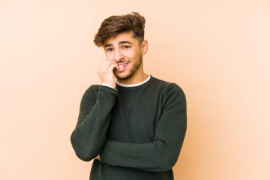 Genç Arap bir adam bej arka planda izole edilmiş tırnak yiyor, gergin ve çok endişeli..