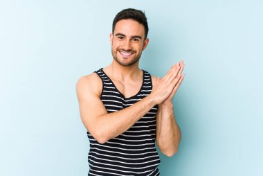 Kafkasyalı genç adam mavi arka planda izole edilmiş enerjik ve rahat hissediyor, ellerini ovuşturuyor kendinden emin.