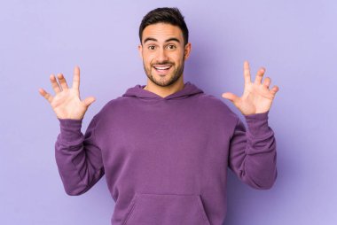 Mor arka planda izole genç beyaz adam hoş bir sürpriz alıyor, heyecanlı ve el kaldırıyor..