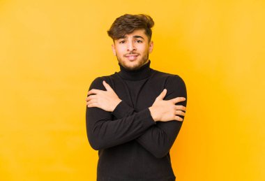 Sarı arka planda izole edilmiş genç bir Arap adam düşük sıcaklıktan ya da hastalıktan soğuyor..
