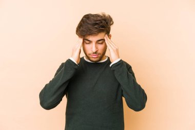 Genç Arap adam bej bir arka planda izole edilmiş tapınaklara dokunuyor ve baş ağrısı çekiyor..