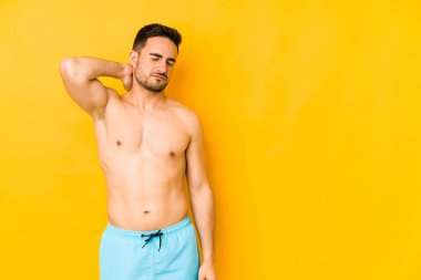 Sarı arka planda mayosu olan genç, beyaz bir adam. Stres yüzünden boynu ağrıyan, masaj yapan ve elle dokunan beyaz bir adam..