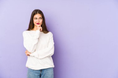 Mor arka planda soyutlanmış beyaz bir kadın şüpheli ve şüpheci bir ifadeyle yana bakıyor..