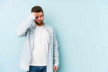 Kafkasyalı genç bir adam mavi arka planda izole edilmiş, başı ağrıyor, yüzüne dokunuyor..