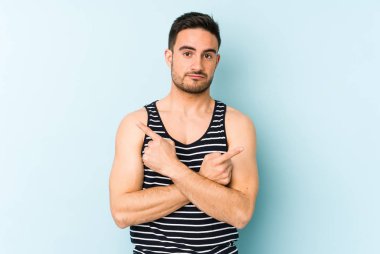 Mavi arka plan noktalarında izole genç beyaz adam, iki seçenek arasında seçim yapmaya çalışıyor.