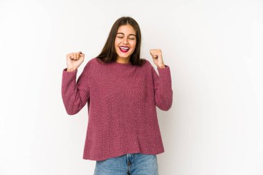 Beyaz arka planda izole edilmiş genç beyaz kadın zaferi, tutkuyu ve coşkuyu kutluyor, mutlu bir ifade..