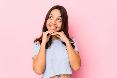 Genç, melez, yalnız bir kadın ellerini çenesinin altında tutuyor ve mutlu bir şekilde yan tarafa bakıyor..