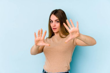 Genç beyaz kadın, mavi arka planda izole edilmiş. Yakın bir tehlike nedeniyle şoka uğruyor.