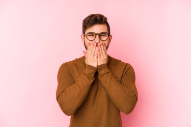 Pembe arka planda izole edilmiş genç beyaz bir adam bir şeye gülüyor, elleriyle ağzını kapatıyor..