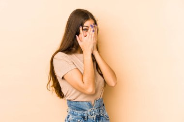 Beyazlı genç bir kadın bej arka planda izole edilmiş. Korkmuş ve gergin parmaklarıyla göz kırp..