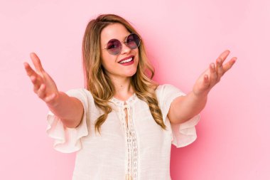 Pembe arka planda gözlüklü genç beyaz kadın zaferi ya da başarıyı kutluyor, şaşırıyor ve şok oluyor..