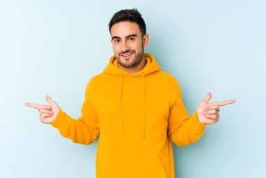 Mavi arka planda izole edilmiş genç beyaz adam farklı kopya alanlarını gösteriyor, birini seçiyor, parmaklarıyla gösteriyor.