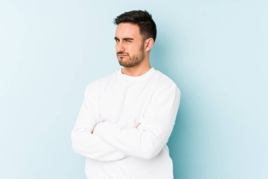 Kafkasyalı genç adam mavi arka planda izole edilmiş şüpheli, belirsiz, seni muayene ediyor..